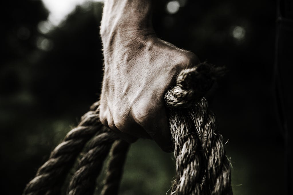 Close-Up of Strong Hand Gripping Rope – Strength & Determination | Photo by Evelyn Chong. Close-up of a strong hand gripping a thick rope outdoors, symbolizing strength, determination, and perseverance.